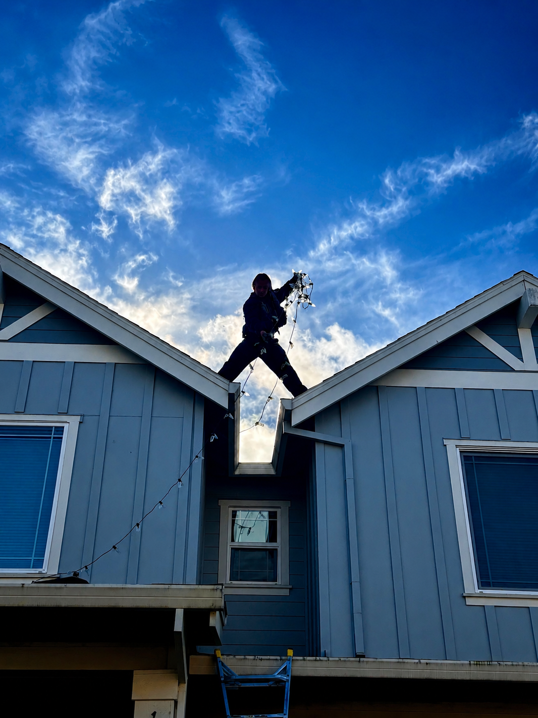 Halen Homes technician installing Christmas lights on a rooftop at sunset