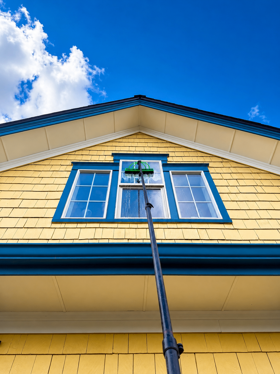 Pole cleaning a gable window on a yellow Oregon farmhouse