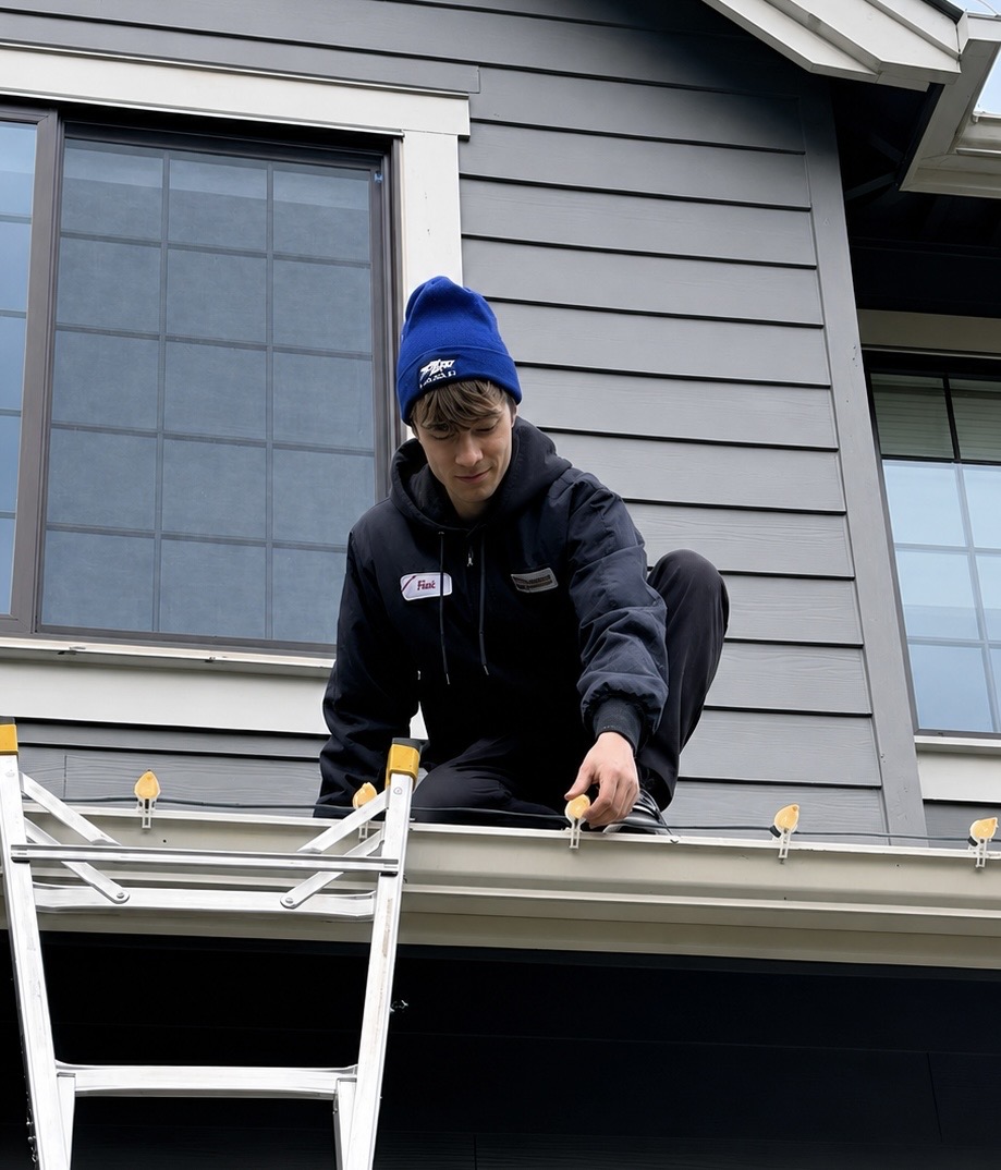 Halen Homes installer clipping bulbs onto a second-story gable during a professional Christmas light installation