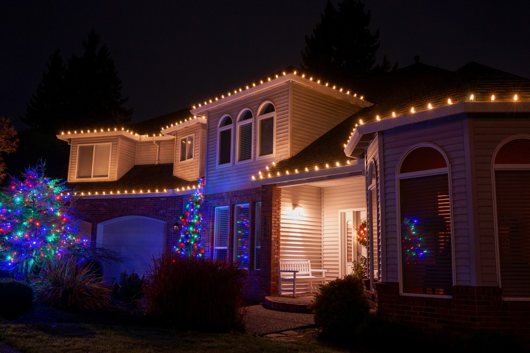 Two-story home outlined in warm-white C9 lights with wrapped trees in multi-color at the entry