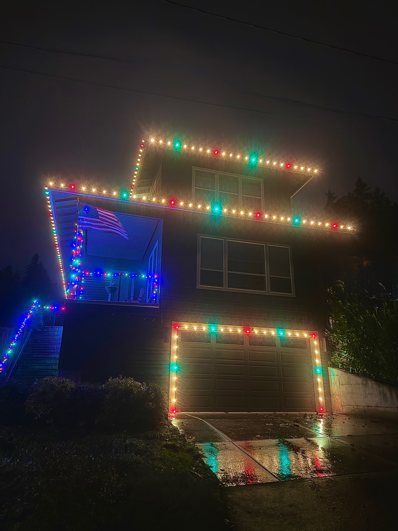 Two-story Oregon home with American flag lit in multi-color and warm-white Christmas lights at night