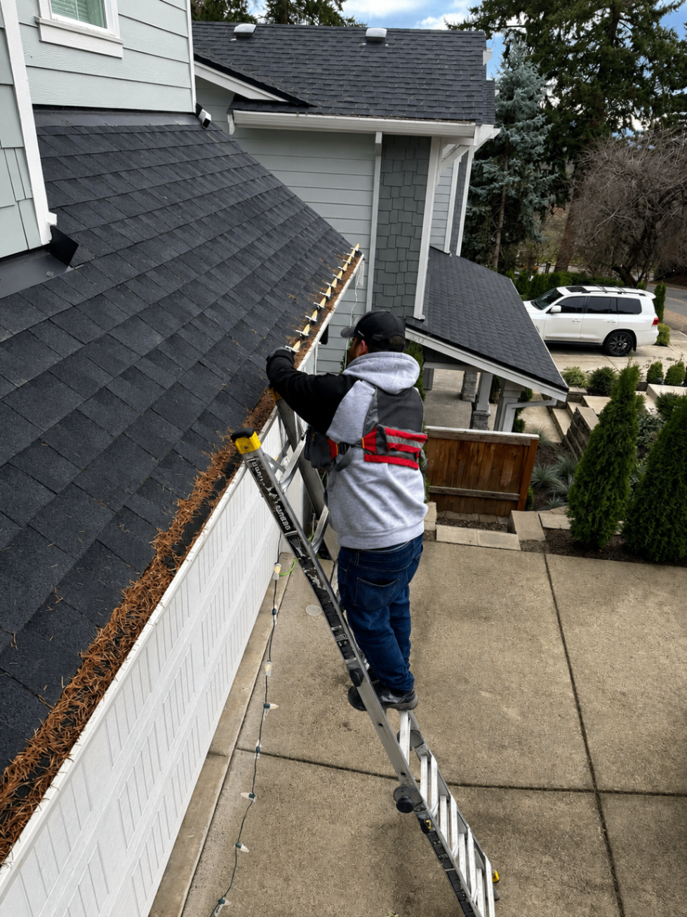 Technician on a ladder installing Christmas lights on a modern grey Oregon home