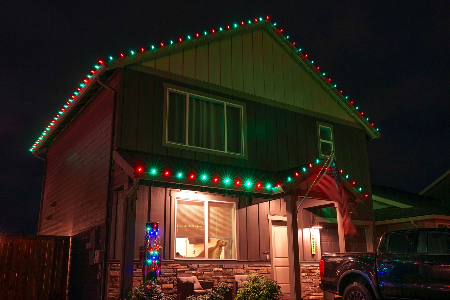 Modern board-and-batten home outlined in classic red and green C9 Christmas lights at night