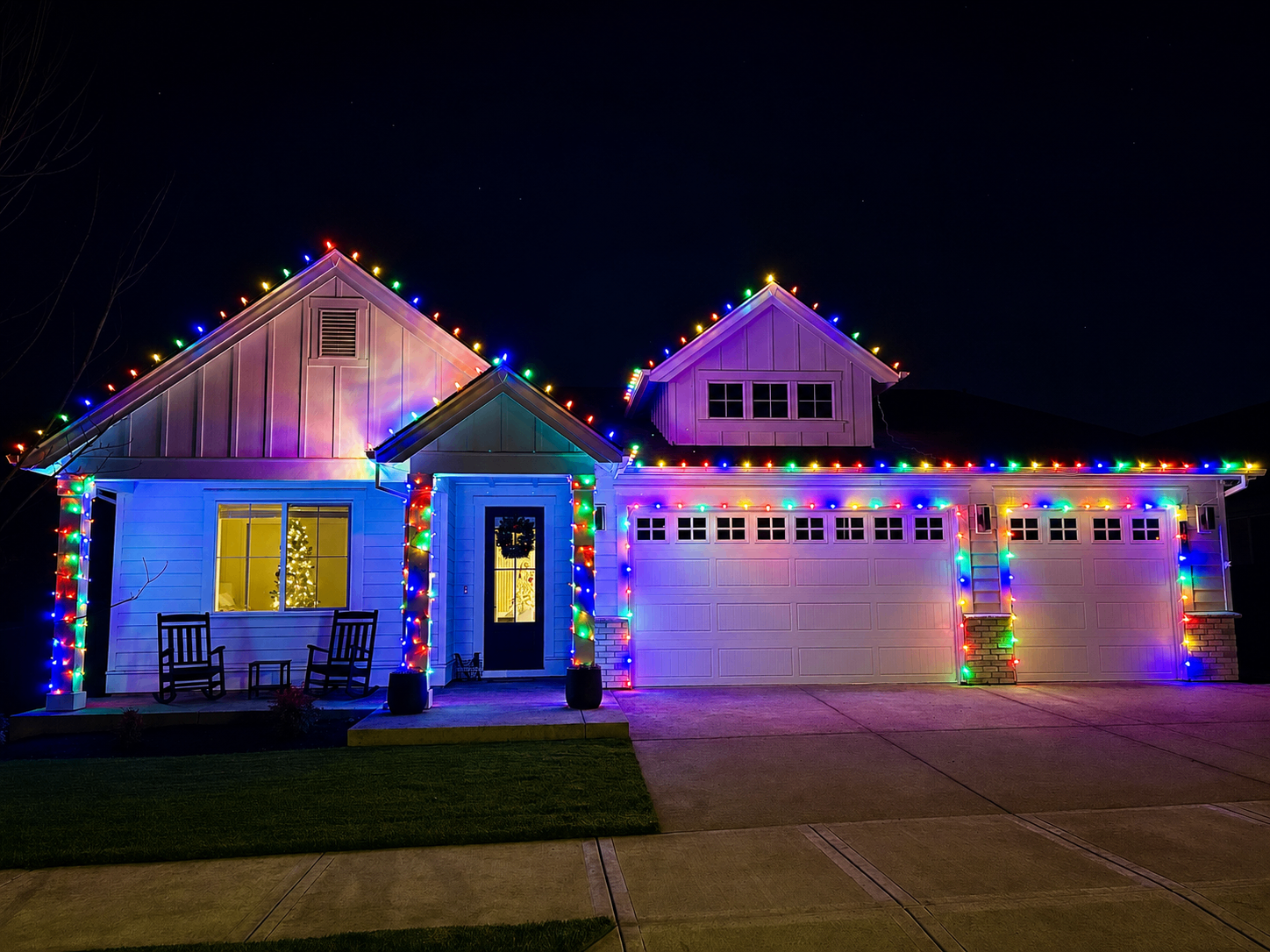 White farmhouse fully outlined in multi-color C9 Christmas lights on peaks, gables and garage