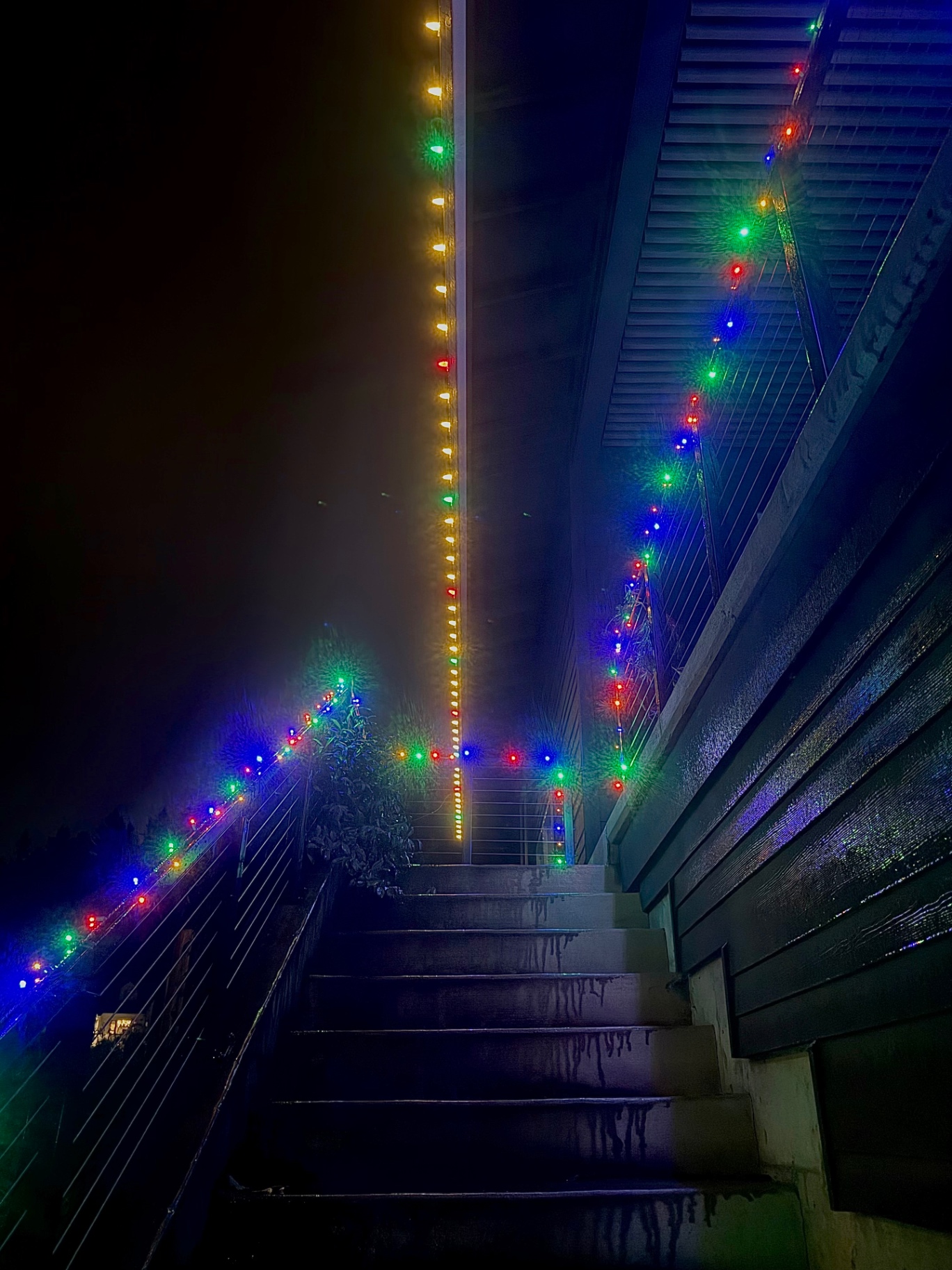 Exterior stairs and railings wrapped in multi-color C9 Christmas lights leading up to a home entry